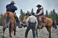 Two men on horseback and a third standing.