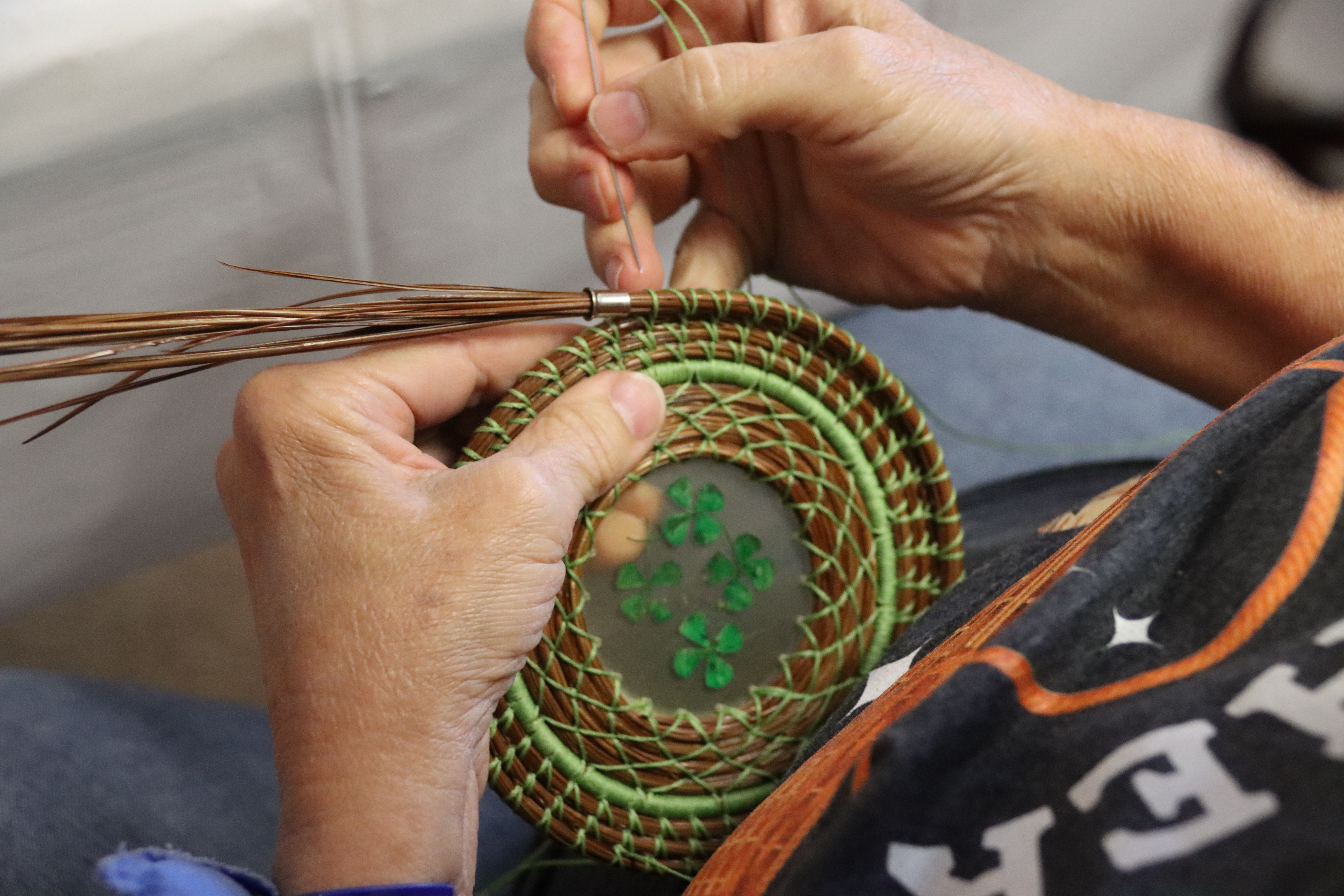 Image shows a Tribal elder weaving a basket using long-leaf pine needles.