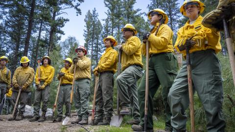 Inter-tribal youth standing in a half circle wearing wildland fire fighter safety closing and hold tools.