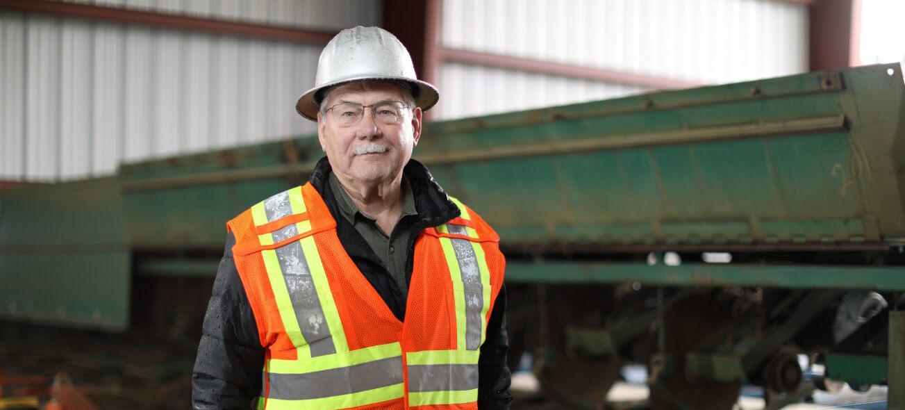 Man in hardhat and safety vest standing near saw mill